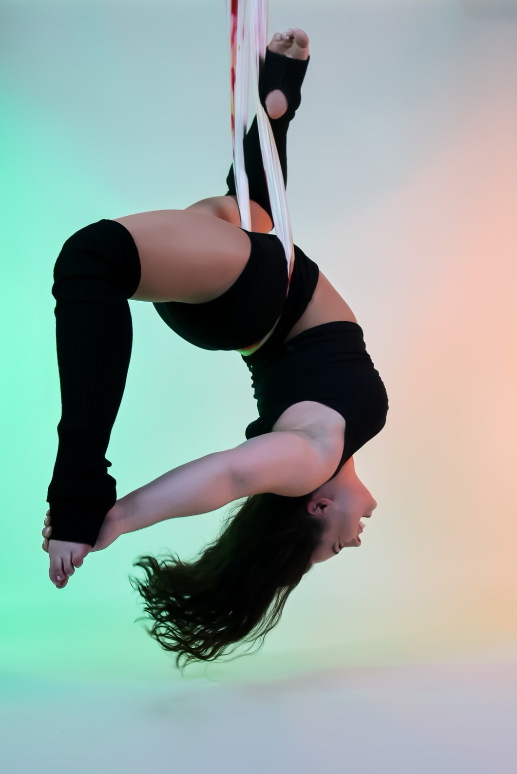 Aerial yoga class — inversions and deep stretch in a soft silk hammock. Student hanging upside down in a white aerial yoga hammock during an aerial yoga class at Flexibility in Flight